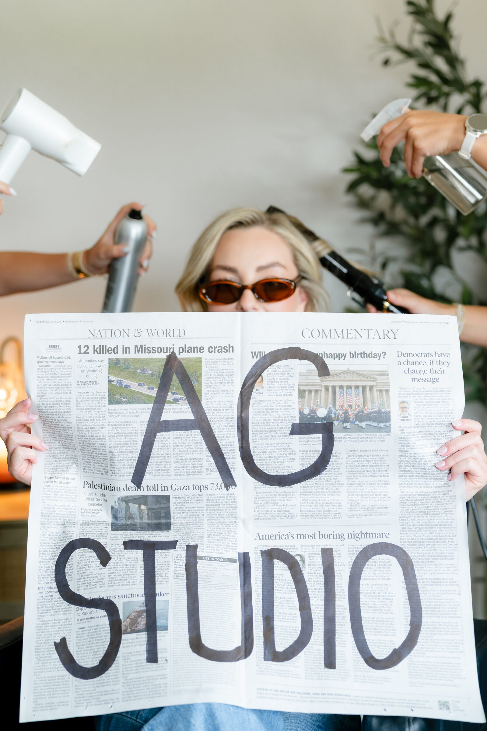A client at AG Studio behind a hand-painted AG Studio newspaper